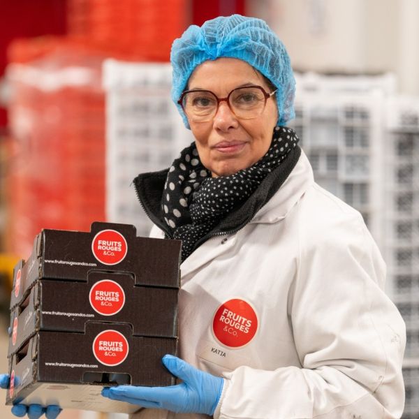 Employée en tenue de laboratoire présentant des boites de fruits rouges